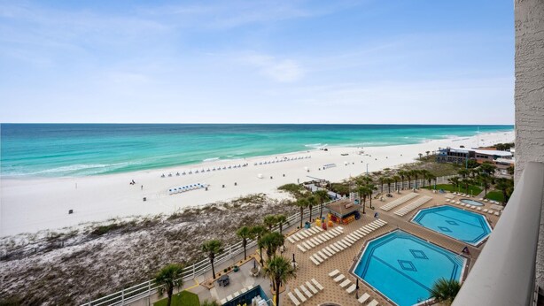 Blick auf einen Strand vom Balkon aus mit Blick auf einen Poolbereich mit Liegestühlen und einem Strand im Hintergrund.