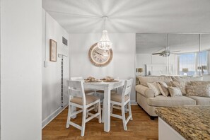 A dining area with a white table and chairs, a wooden clock, and a chandelier. - Top of The Gulf 213 (Panama City Beach)