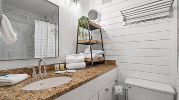 A bathroom with a granite countertop, a sink, a mirror, a towel rack, and a shelf with towels and a plant.