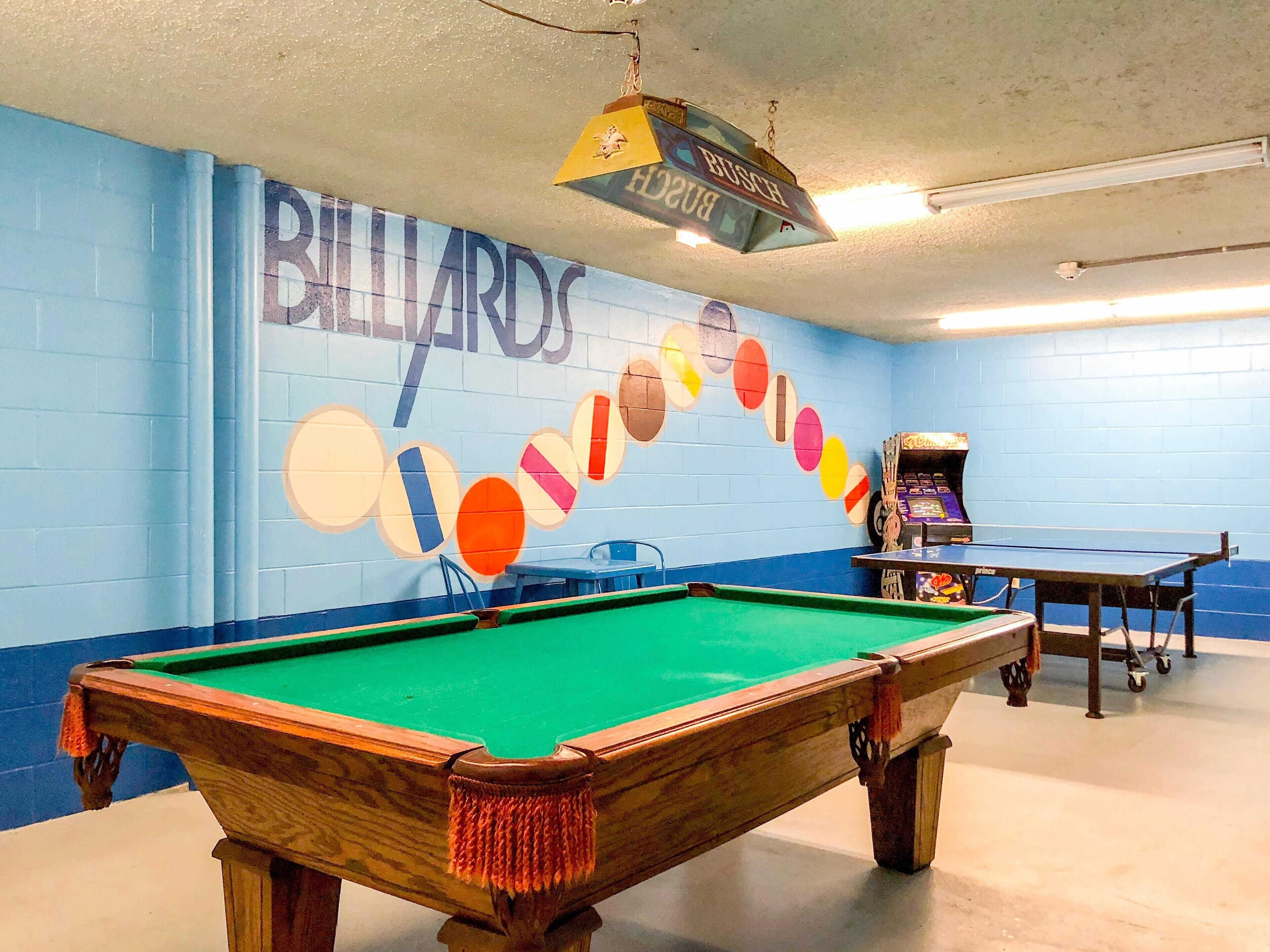 A billiards room with a pool table, a table tennis table, and a mural with colorful circles.