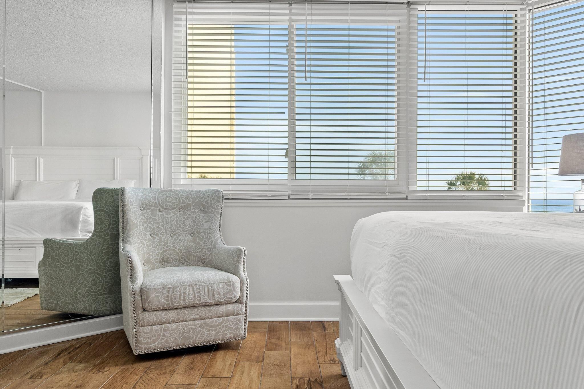 Ein Schlafzimmer mit Bett, Sessel und einem Fenster mit Jalousien.