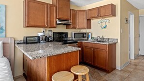Una cocina compacta con armarios de madera, encimeras de granito, microondas, tostadora y cafetera.