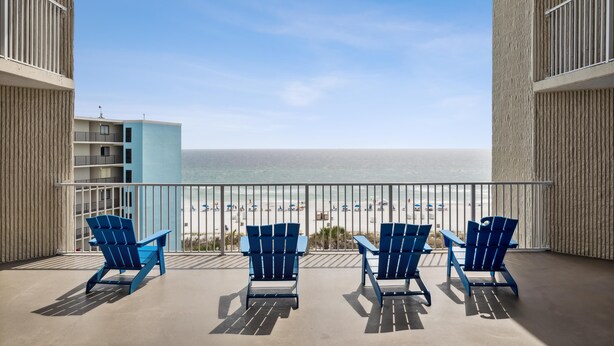 Een balkon met drie blauwe Adirondack stoelen gericht op een strand.