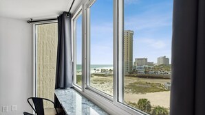 Een kamer met een groot raam met uitzicht op een strand en de skyline van de stad.