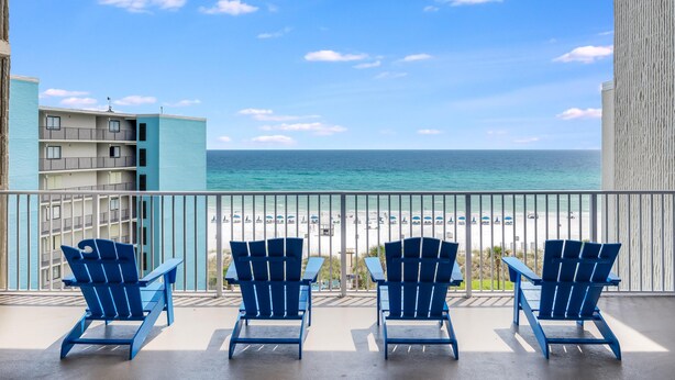 Ein Balkon mit drei blauen Adirondack-Stühlen mit Blick auf einen Strand.