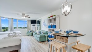 Ein modernes Hotelzimmer mit einem großen Bett, einer Sitzecke mit einem grünen Sofa, einer Küchenzeile mit einem runden Tisch und einem Deckenventilator.