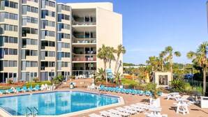 Ein Hotel mit Swimmingpool, Liegestühlen und Palmen.