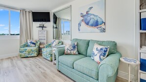 Ein Wohnzimmer mit einem grünen Sofa, passendem Hocker und einem Gemälde mit Schildkrötenmotiv.
