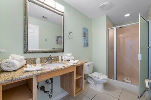 A bathroom with a granite countertop sink, a large mirror, a toilet, and a glass-enclosed shower. - Splash 804e (Panama City Beach)