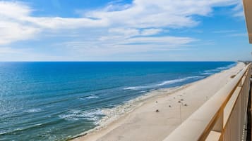 Vista da praia a partir de uma varanda, com céu claro e mar calmo.