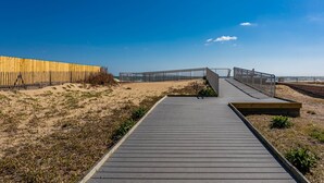 Una passerella in legno che conduce a una spiaggia, con una recinzione in legno da un lato e una ringhiera metallica dall'altro.