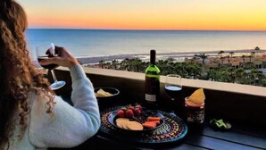 En person sitter vid ett bord med utsikt över havet, en vinflaska och en tallrik med tilltugg.