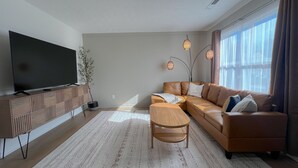A modern living room with a large flat-screen TV, a leather sofa, a wooden coffee table, and a patterned rug. - Olive Tree Oasis - 10 Minutes to the Ark!
 (Dry Ridge)