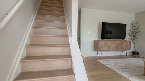 A staircase with wooden steps and white handrails, leading to a room with a flat-screen TV and a wooden bench. - Olive Tree Oasis - 10 Minutes to the Ark!
 (Dry Ridge)