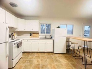 Compact kitchen with stove, sink, and refrigerator, featuring a casual dining area with stools.