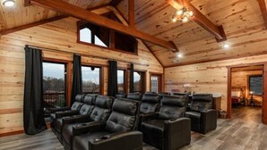 Un'ampia stanza con pareti in legno e soffitto spiovente, con un'area salotto dotata di poltrone in pelle e un'ampia finestra che offre vista sull'esterno.