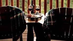 Una mesa con dos sillas en una terraza de madera, con vistas a un paisaje montañoso.