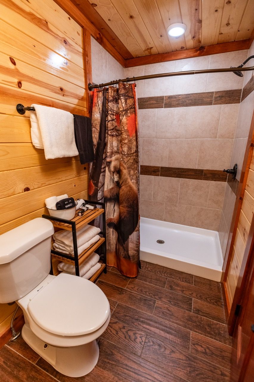 Ein Badezimmer mit Holzwandverkleidung, Toilette, Dusche und Handtuchhalter.