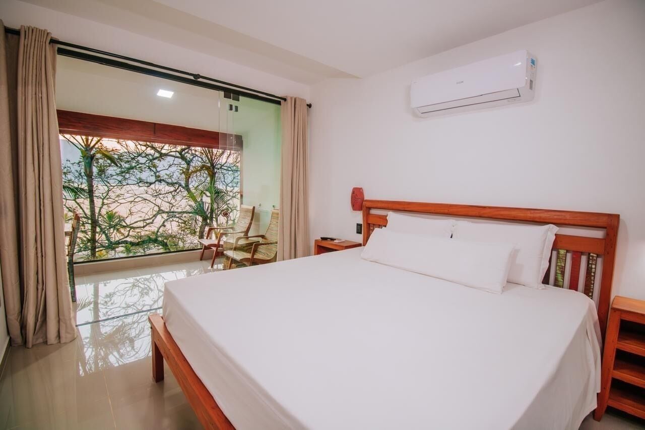 A hotel room with a large bed, a wooden headboard, a nightstand, and a window with curtains.