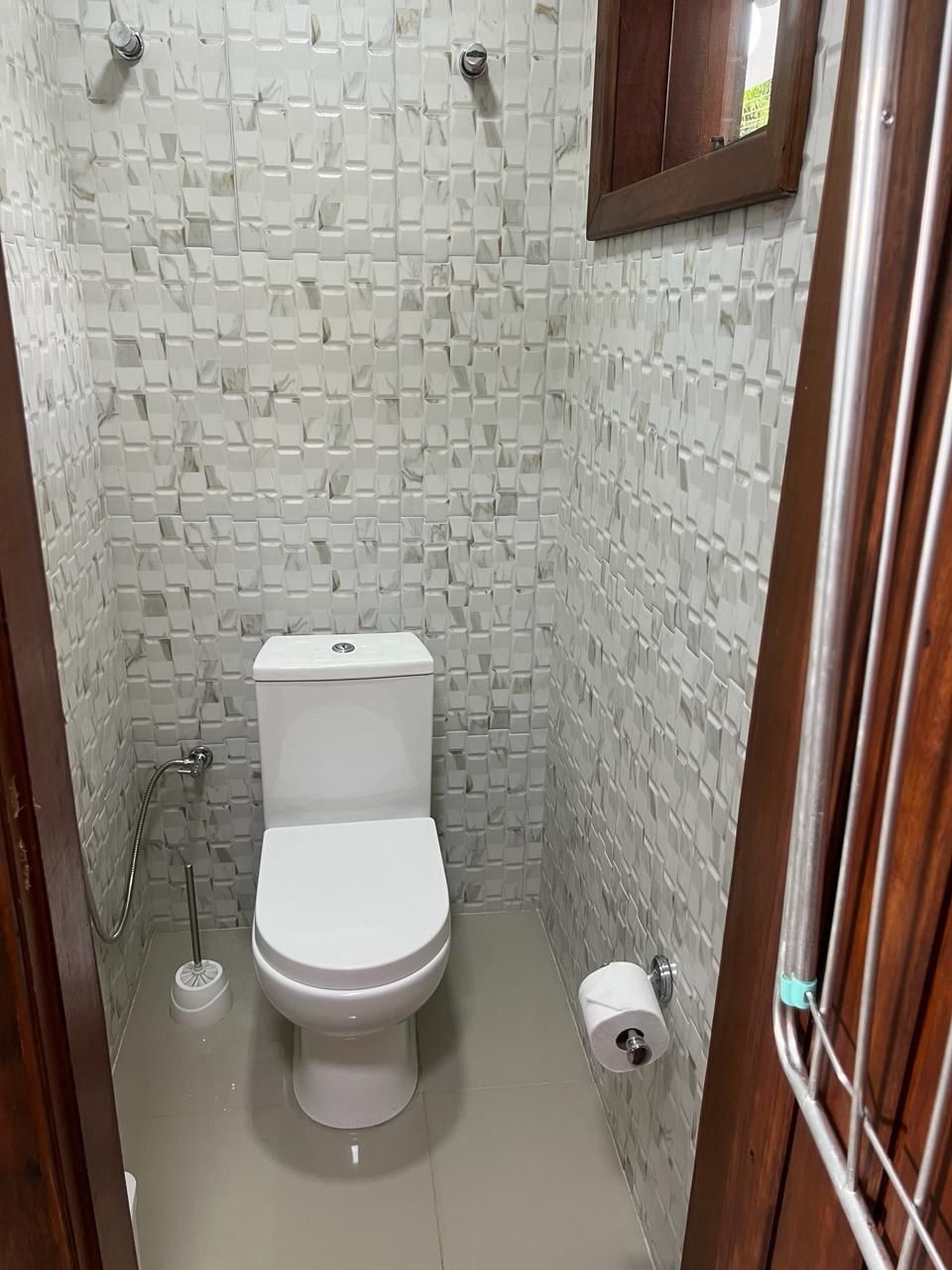 A small, tiled bathroom with a toilet, a toilet paper holder, and a showerhead.