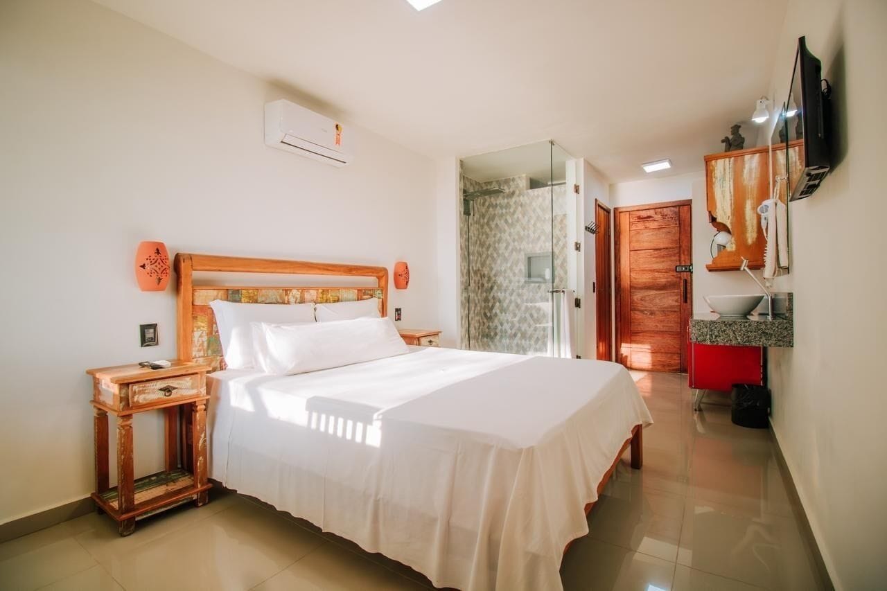 A bedroom with a wooden bed, a bedside table, a TV, and a bathroom visible through an open door.