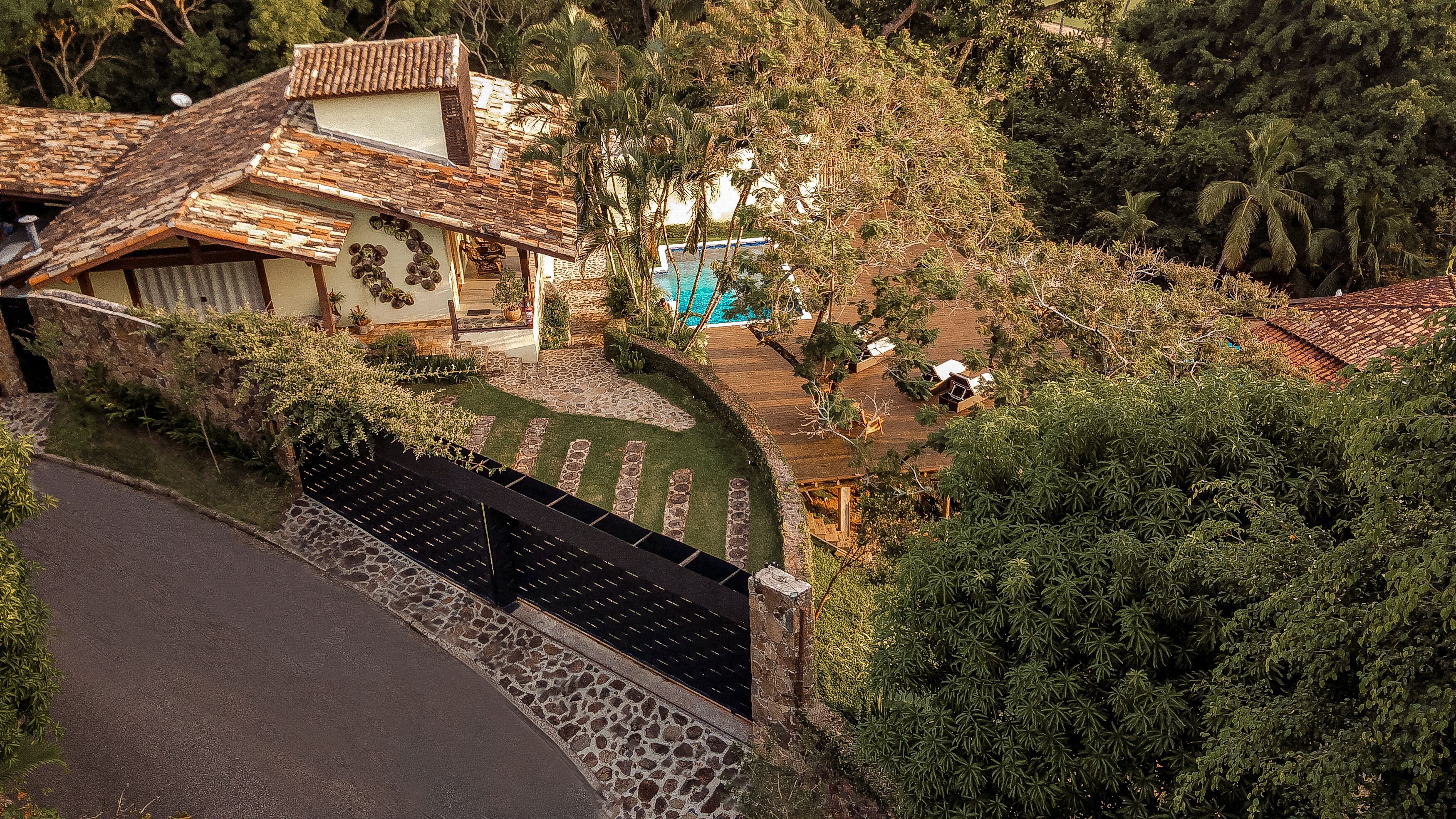 Uma vila com um caminho de pedra que leva a uma piscina, cercada por vegetação exuberante e vista para o mar.