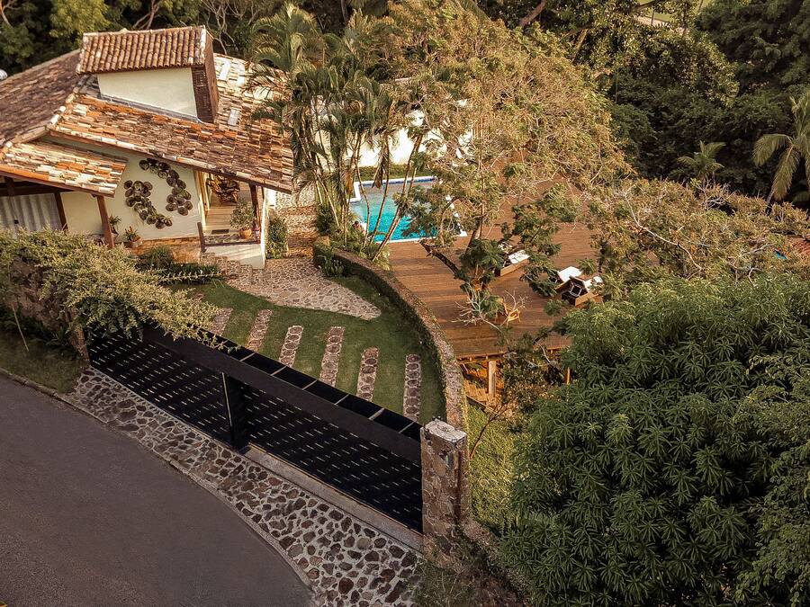 Uma vila com um caminho de pedra que leva a uma piscina, cercada por vegetação exuberante e vista para o mar.