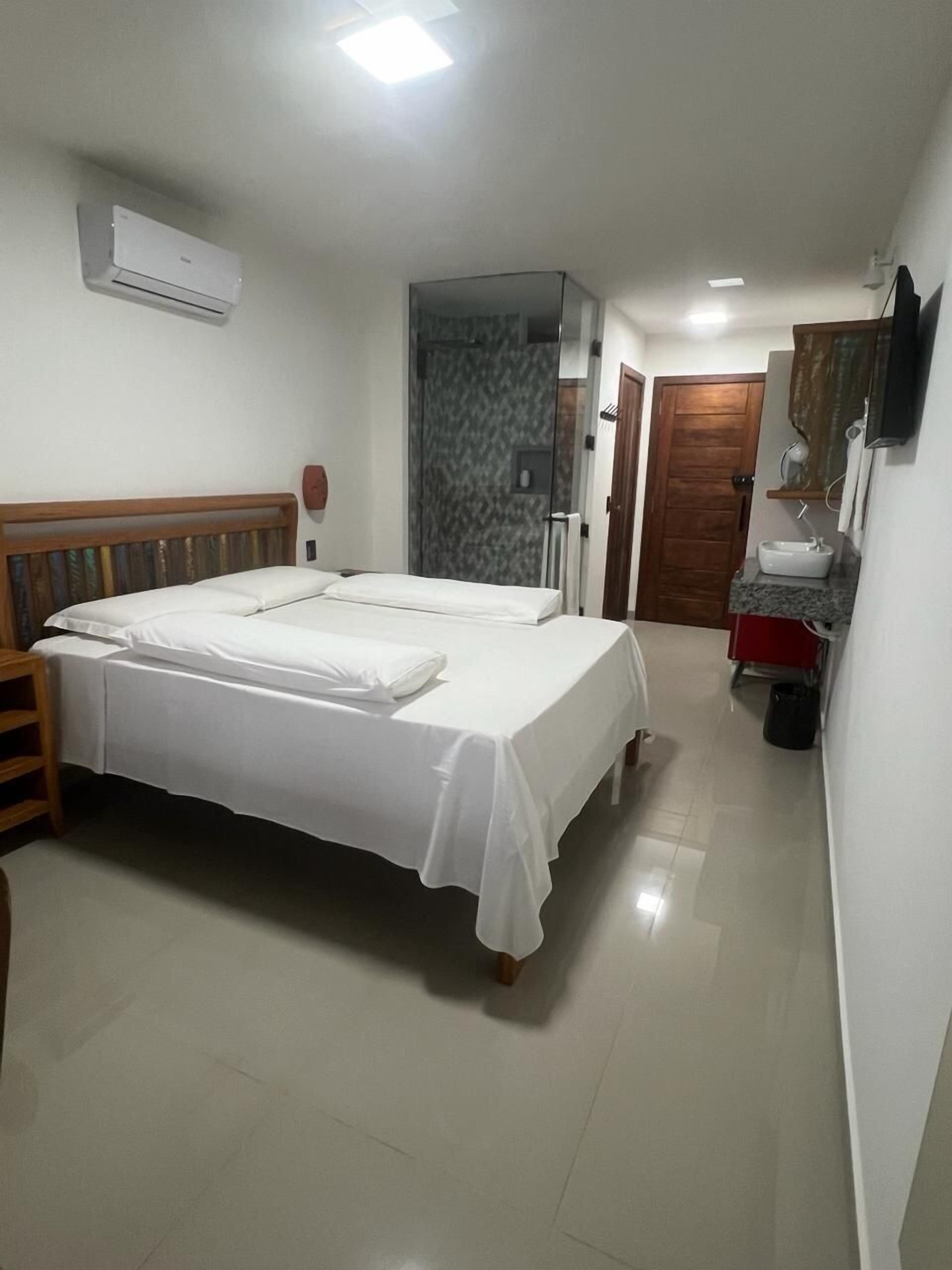 A bedroom with a bed, a bedside table, a mirror, a sink, and a shower area.