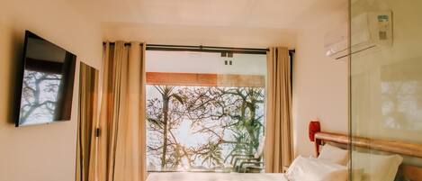 Een hotelkamer met een bed, een aan de muur bevestigde televisie en een groot raam met gordijnen.