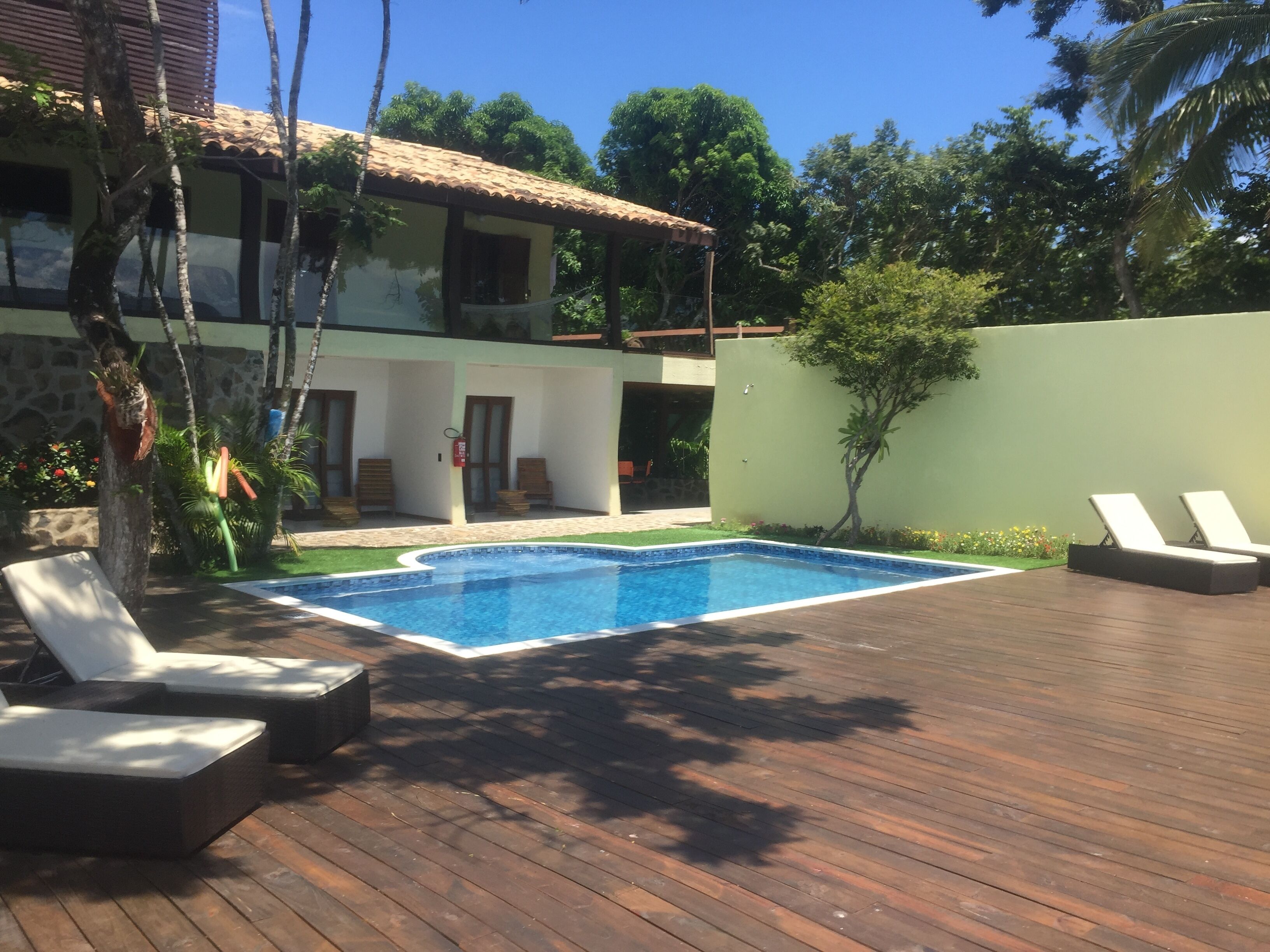 A wooden deck with a swimming pool, lounge chairs, and a stone wall.