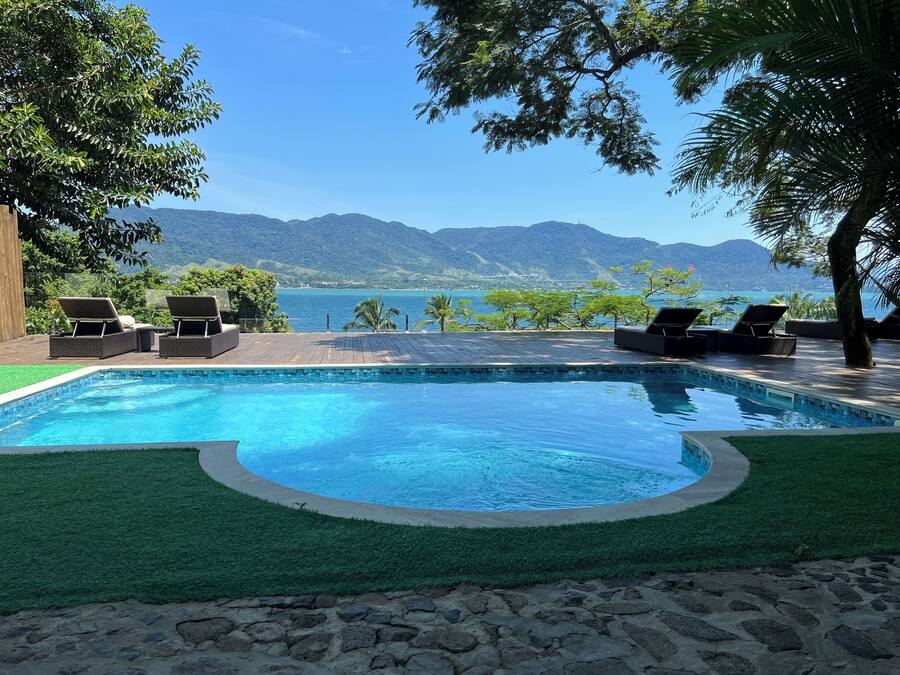 Piscina com espreguiçadeiras e vista para montanhas e um corpo de água.