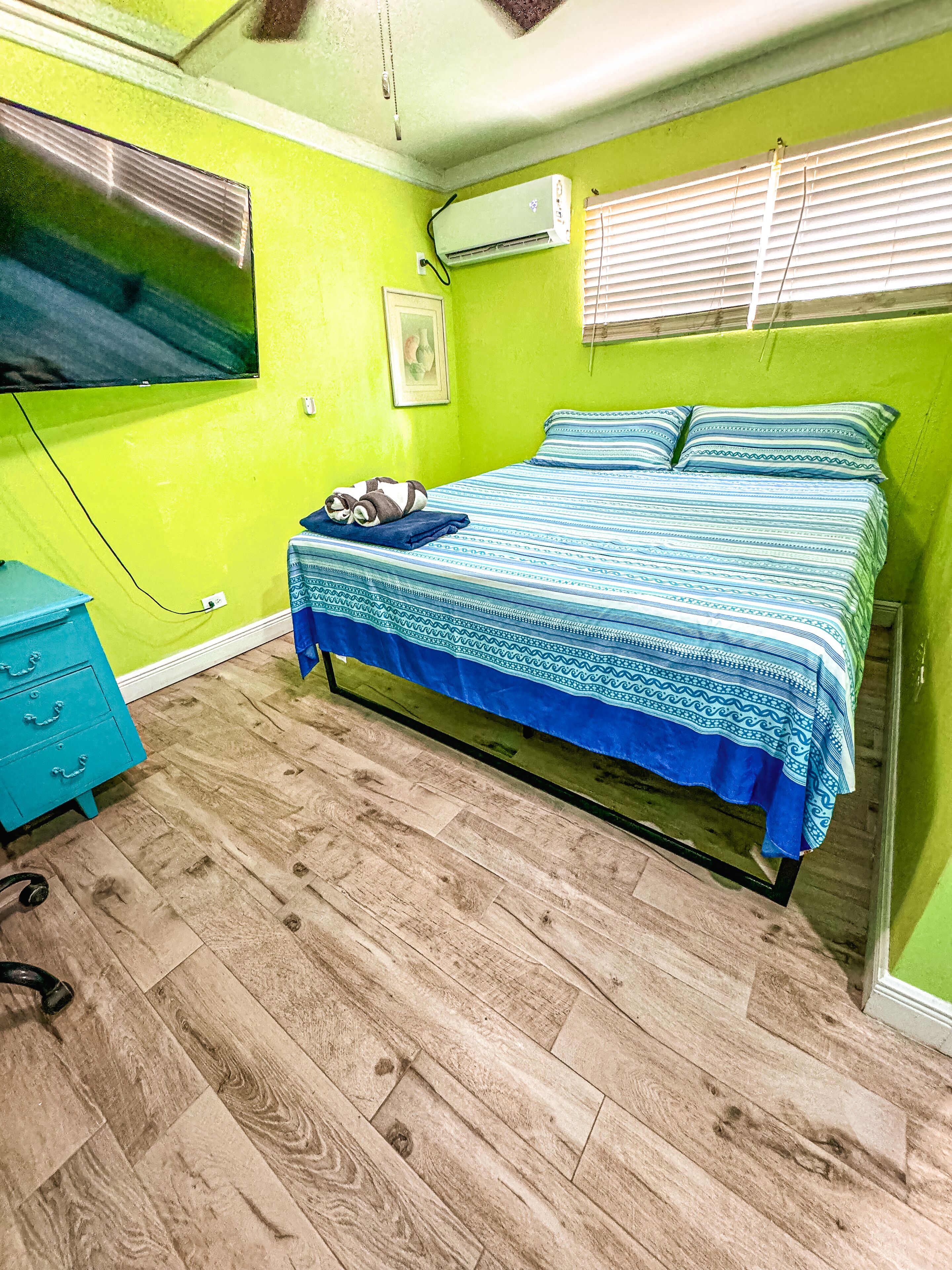 Een slaapkamer met een bed, een blauwe dressoir en een raam met jaloezieën.