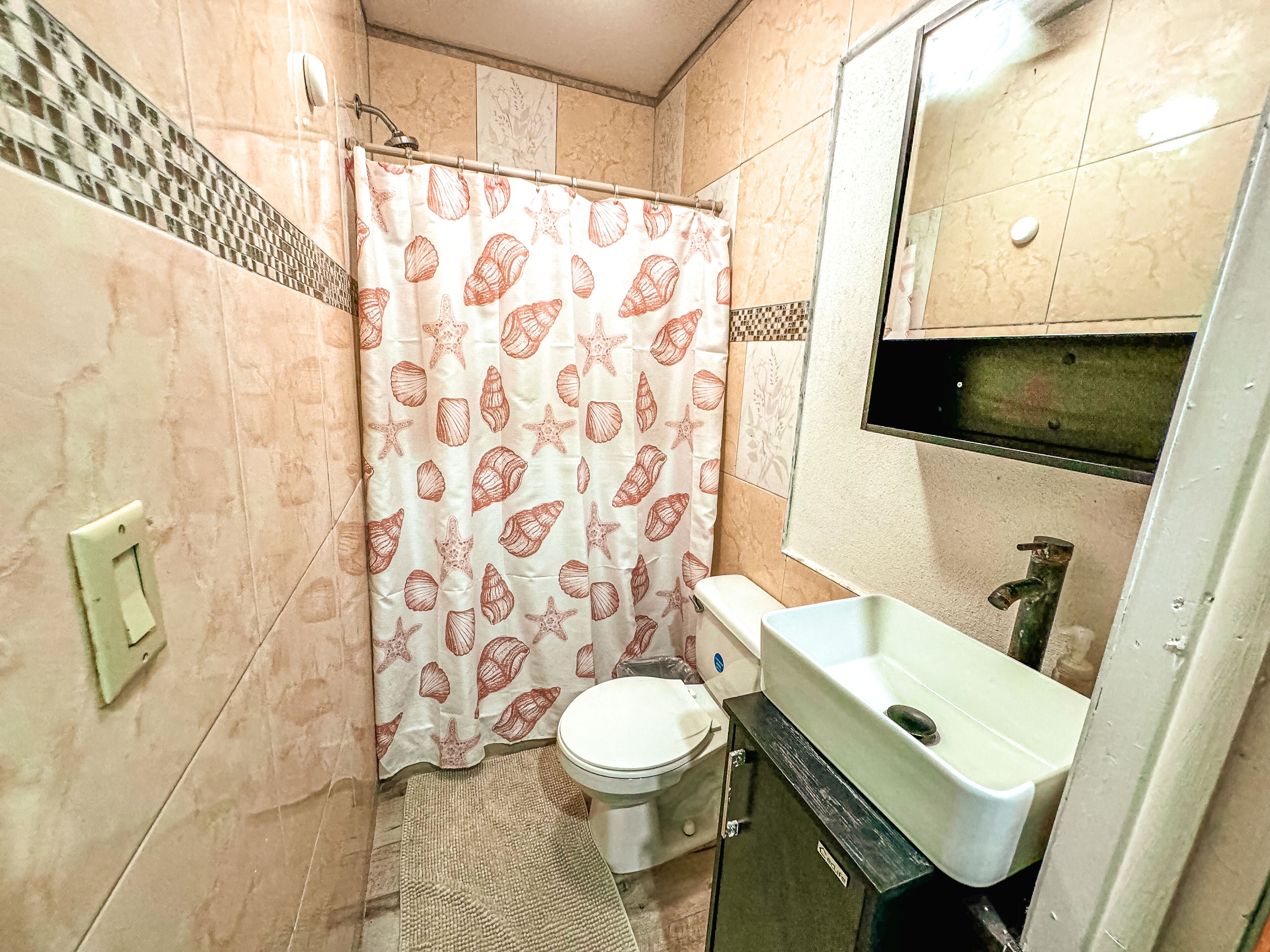 Ein Badezimmer mit Toilette, Waschbecken und Duschvorhang mit Muschelmuster.