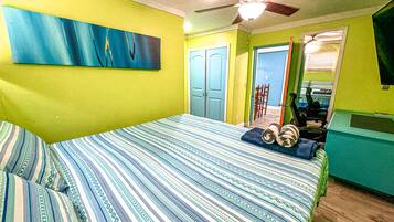 A bedroom with a bed, a ceiling fan, and a door leading to another room.