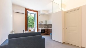 A modern apartment with a grey sofa, a kitchen with wooden cabinets, and a white door. - Loft Piazza Marina (Palermo)