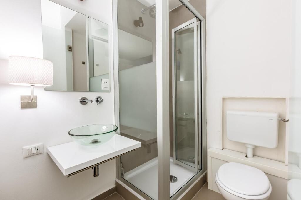 Ein modernes Badezimmer mit einem Waschbecken aus Glas, einer Toilette und einer begehbaren Dusche.