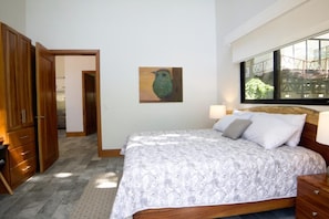 A bedroom with a bed, a wooden wardrobe, a painting on the wall, and a window with a view of a building.