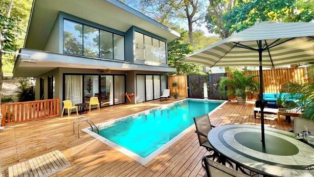 Ein modernes Haus mit Schwimmbad, Holzterrasse und Gartenmöbeln.