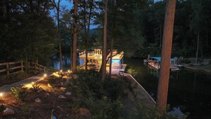 A lakeside cabin with a deck and outdoor lighting, surrounded by trees and a dock.