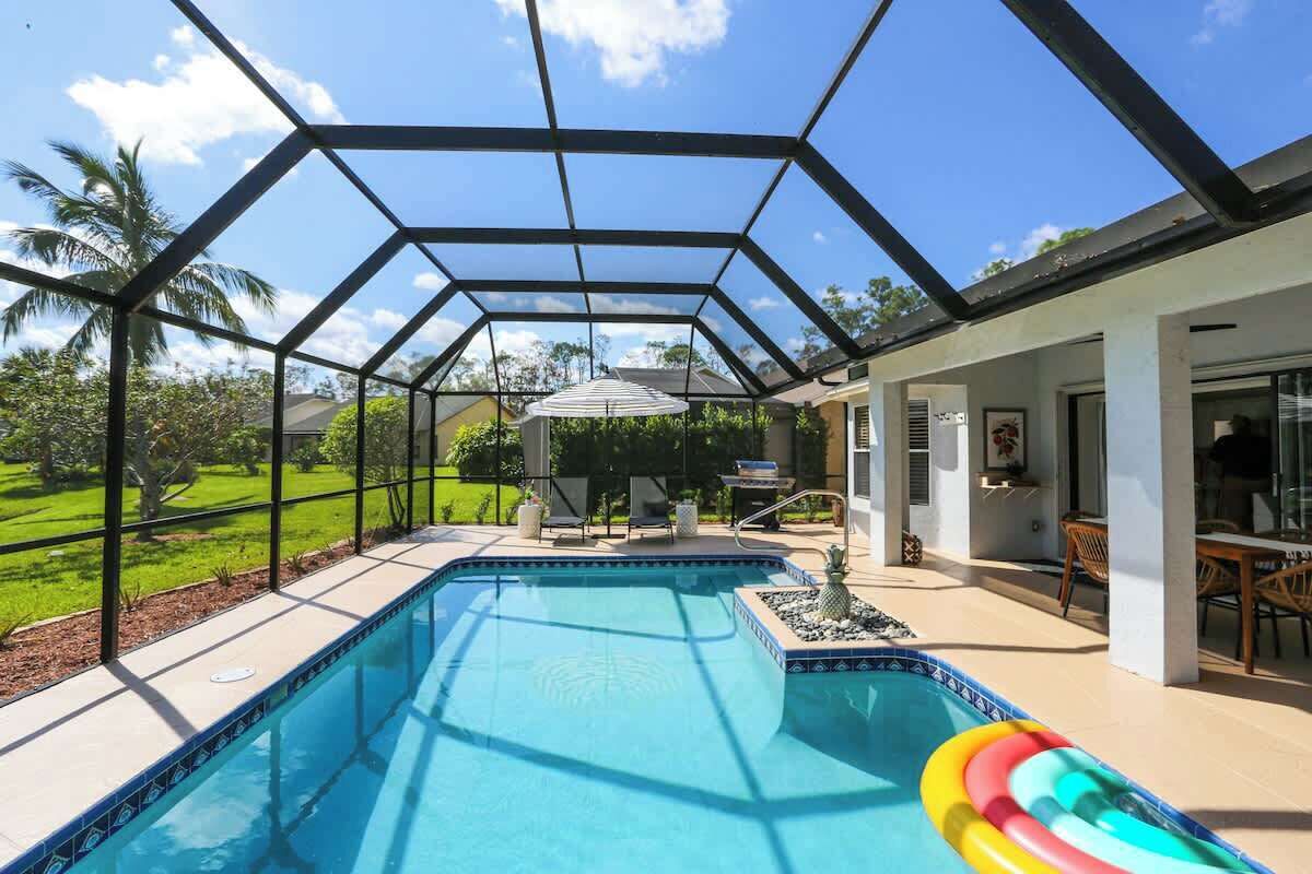 Une piscine couverte dotée d’une structure de toit aux lignes géométriques, entourée d’un patio aménagé avec du mobilier d’extérieur et offrant une vue sur un jardin luxuriant.