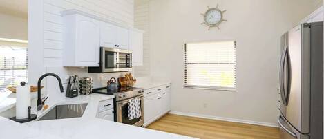 A modern kitchen with white cabinetry, stainless steel appliances, and a wooden floor.