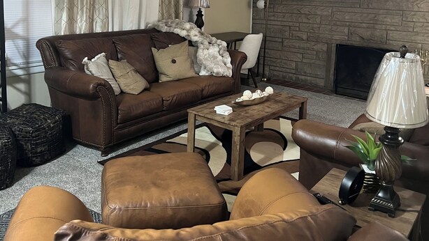 A living room with a brown leather sofa, a coffee table, and a television mounted on a stone wall. -  Looking for relaxation and comfort? Look no further with all its amenities.  (Indianapolis)