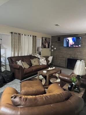 A living room with a brown leather sofa, a coffee table, and a television mounted on a stone wall.