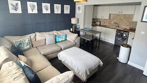 A modern living room with a sectional sofa, a dining area, and a kitchen with a washing machine. - Beautiful 2-bed Apartment in Rhosneigr (Rhosneigr)