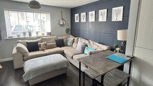 A modern living room with a sofa set, a dining table, and a large window. - Beautiful 2-bed Apartment in Rhosneigr (Rhosneigr)