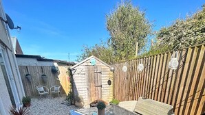 A patio area with wicker furniture, a small shed, and a wooden fence. - Beautiful 2-bed Apartment in Rhosneigr (Rhosneigr)