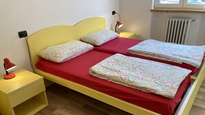 A double bed with red bedding and heart-patterned pillows, a bedside table with a red lamp, and a radiator in the background. - Bikeapt Two-bedroom apartment 3 with lake view and private parking a stone's throw from downtown (Malcesine)