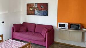 A living room with a pink sofa, a table with a patterned tablecloth, a wall-mounted artwork, and a microwave on a shelf. - Bikeapt Two-bedroom apartment 3 with lake view and private parking a stone's throw from downtown (Malcesine)