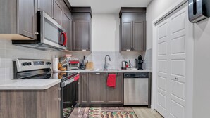 A modern kitchen with dark wood cabinets, stainless steel appliances, and a white tiled backsplash. - Beautiful Modern Unique Suite (Calgary)