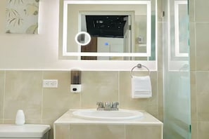 Un baño moderno con un espejo grande, un lavamanos y una cabina de ducha con paredes de vidrio.